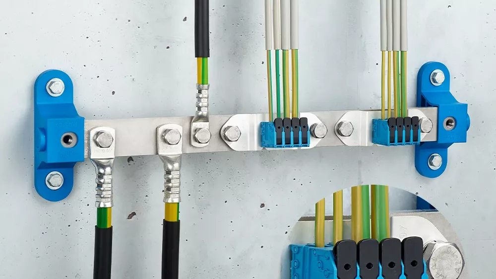 Metal grounding bar on a wall with black and white cables, green-yellow conductors, blue terminal blocks, and blue mounting brackets.