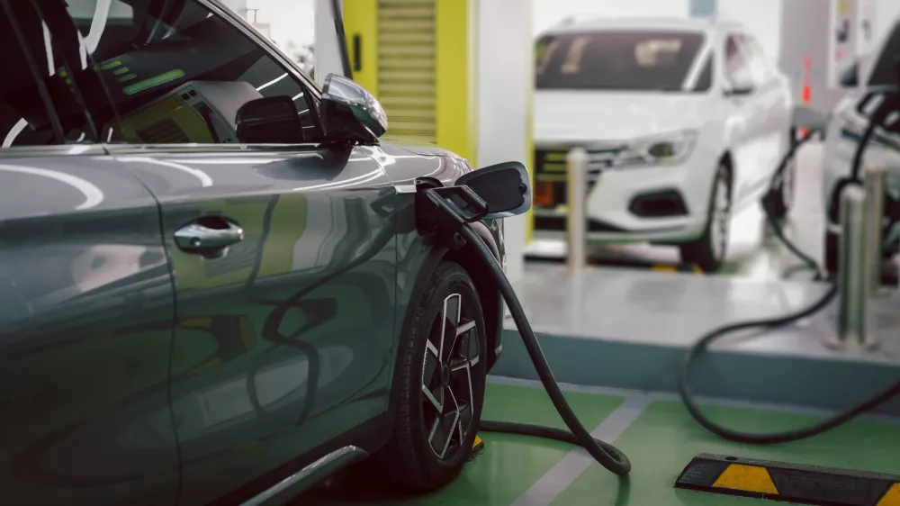 Electric car charging at indoor EV charging station, plug connected to vehicle with another electric car in background.