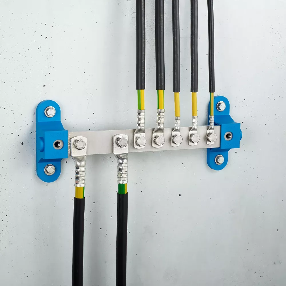 Wall-mounted grounding bar with metal terminals and connected black and yellow-green cables on a light gray wall.