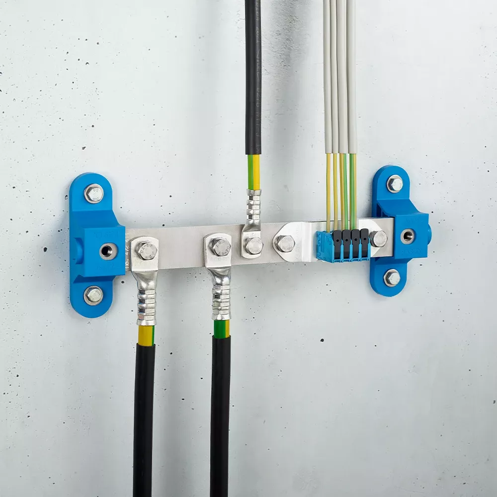 Wall-mounted grounding bar with metal terminals and connected black and yellow-green cables on a light gray wall.